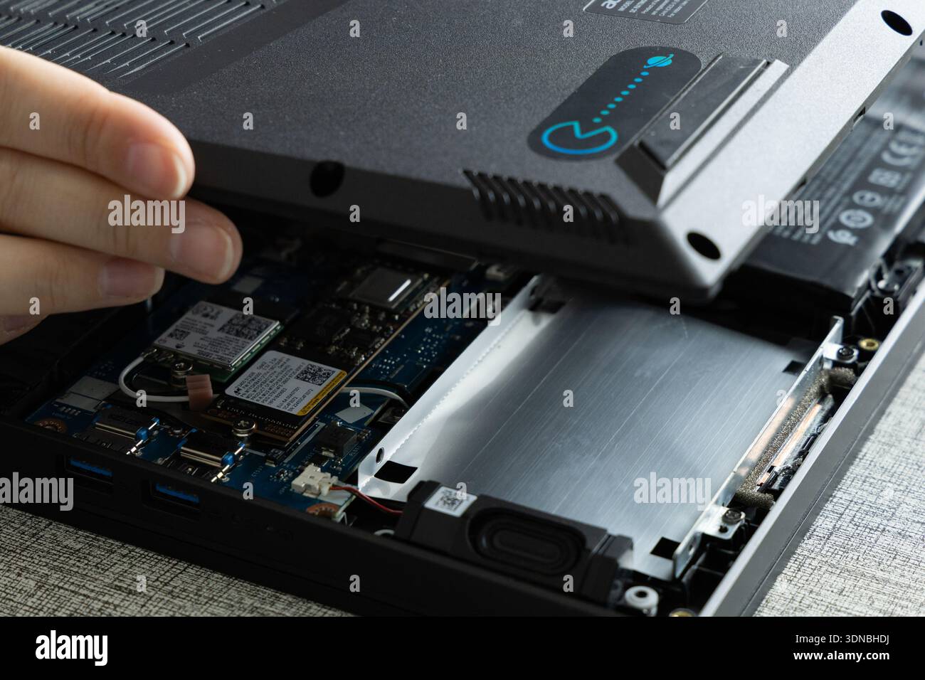 Una mano solleva il coperchio di un notebook, rivelandone le parti interne. L'area di lavoro ha uno sfondo semplice. Foto Stock