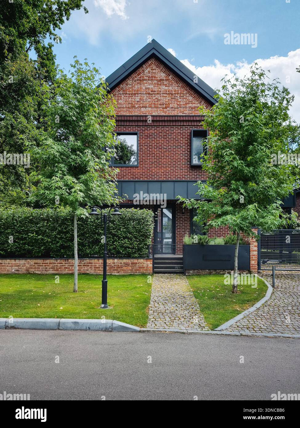 Moderna casa in mattoni rossi immersa nel verde. Residence a due piani con tetto a tegole e accenti in metallo nero. Prato verde e passerella di ciottoli conducono all'ingresso. Foto Stock