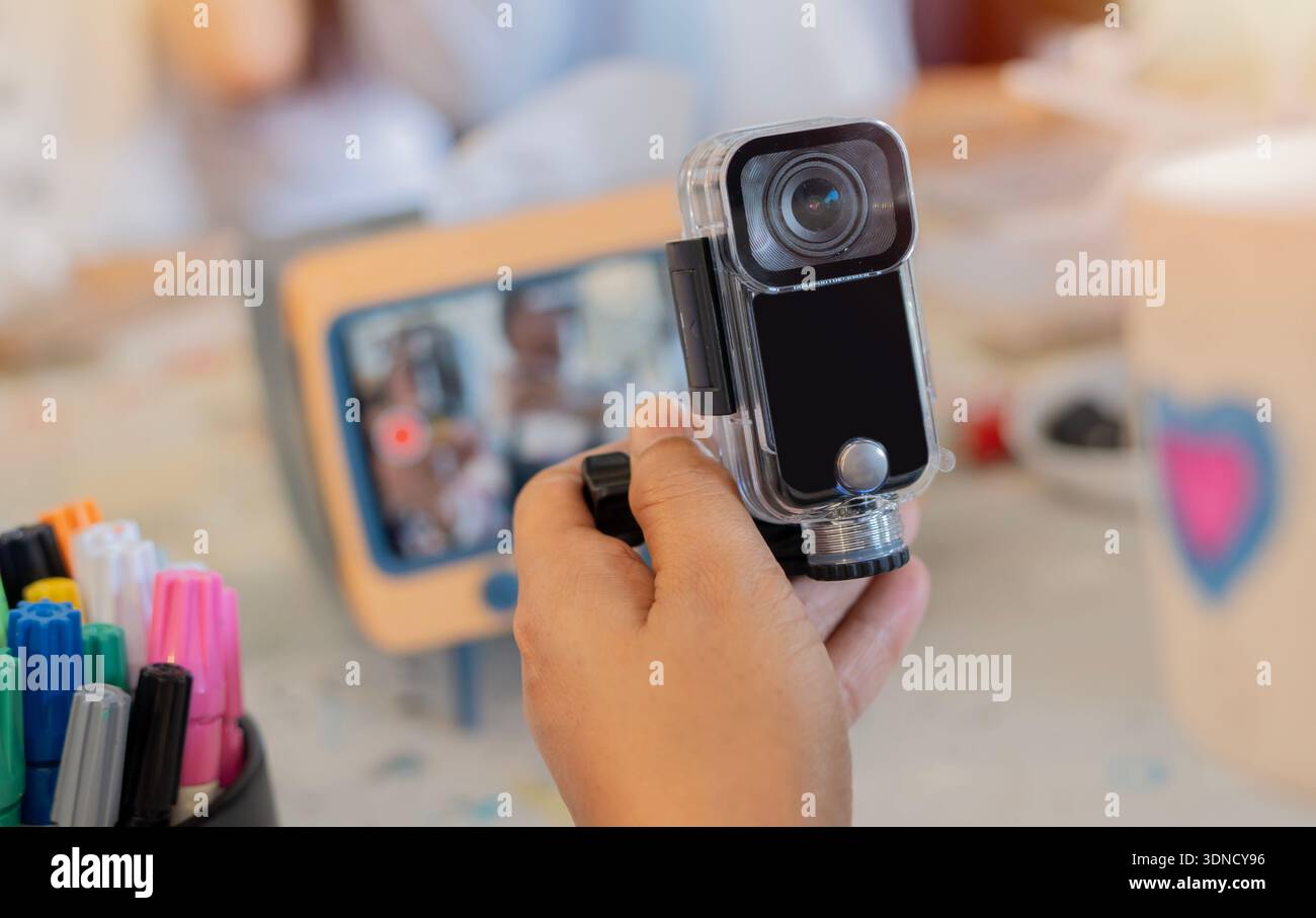Una piccola action camera sulle mani di una giovane donna seduta su un tavolo d'arte. Messa a fuoco selettiva. Concetto di Action camera. Foto Stock