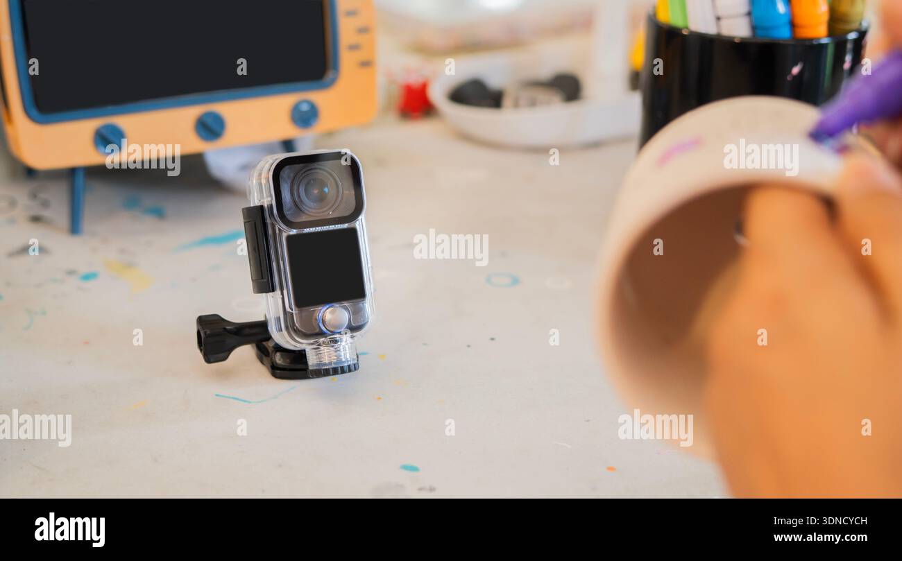 Influencer che crea contenuti per workshop artistici con una action camera, ambientata su un tavolo artistico. Messa a fuoco selettiva sul soggetto. Foto Stock