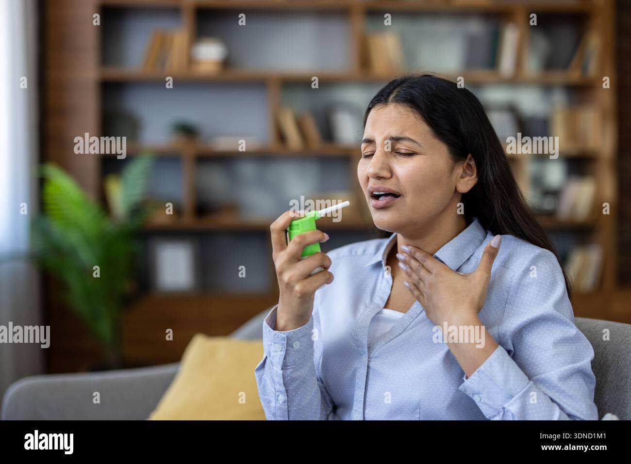 Giovane donna indiana che prova una sensazione grezza o graffiante nella gola, usando uno spray medicato per un rapido sollievo dai sintomi della malattia e disagio a casa Foto Stock