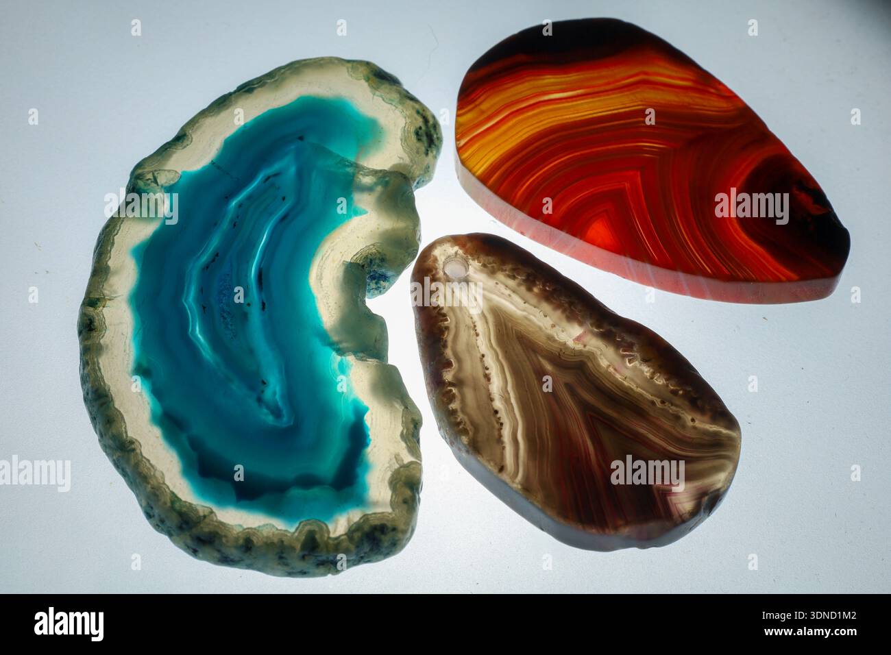 tre pietre di agata lucidate in tonalità blu, rosso e marrone illuminate da dietro per rivelare le strutture interne. Foto Stock