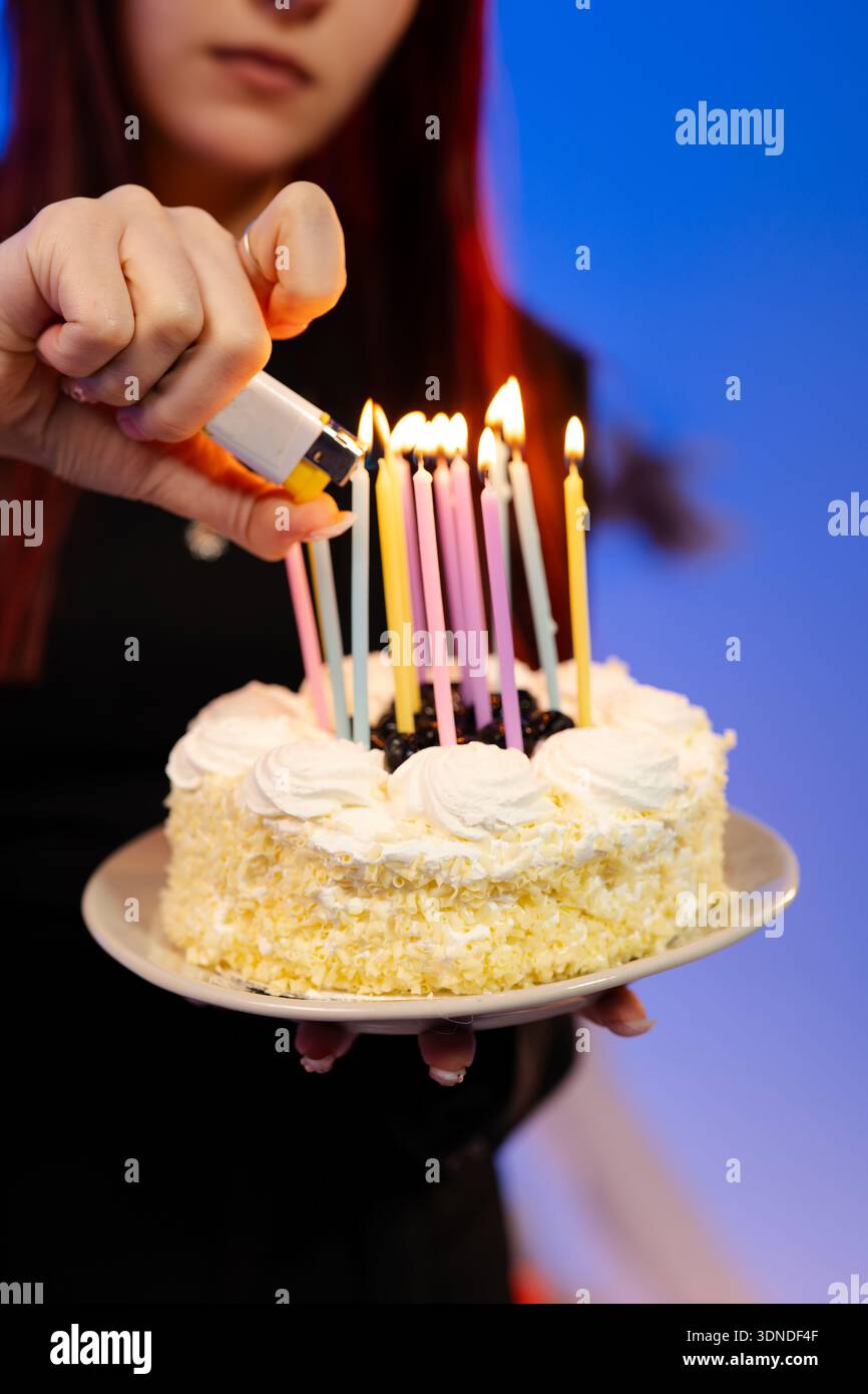 La mano della donna accende le candele su una torta di compleanno da vicino Foto Stock