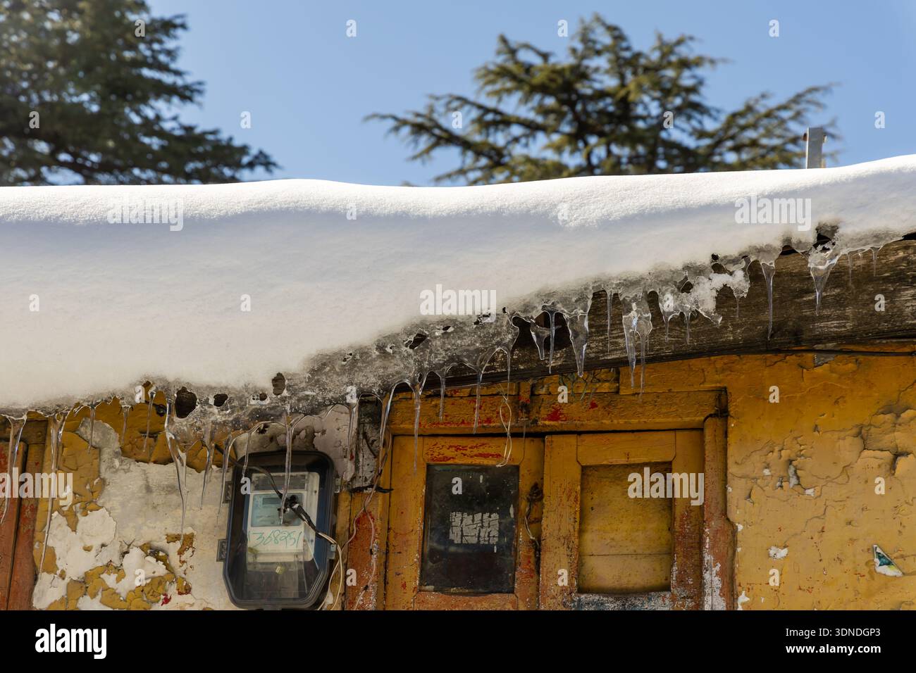 tetto innevato con ghiaccioli affilati contro il cielo blu Foto Stock
