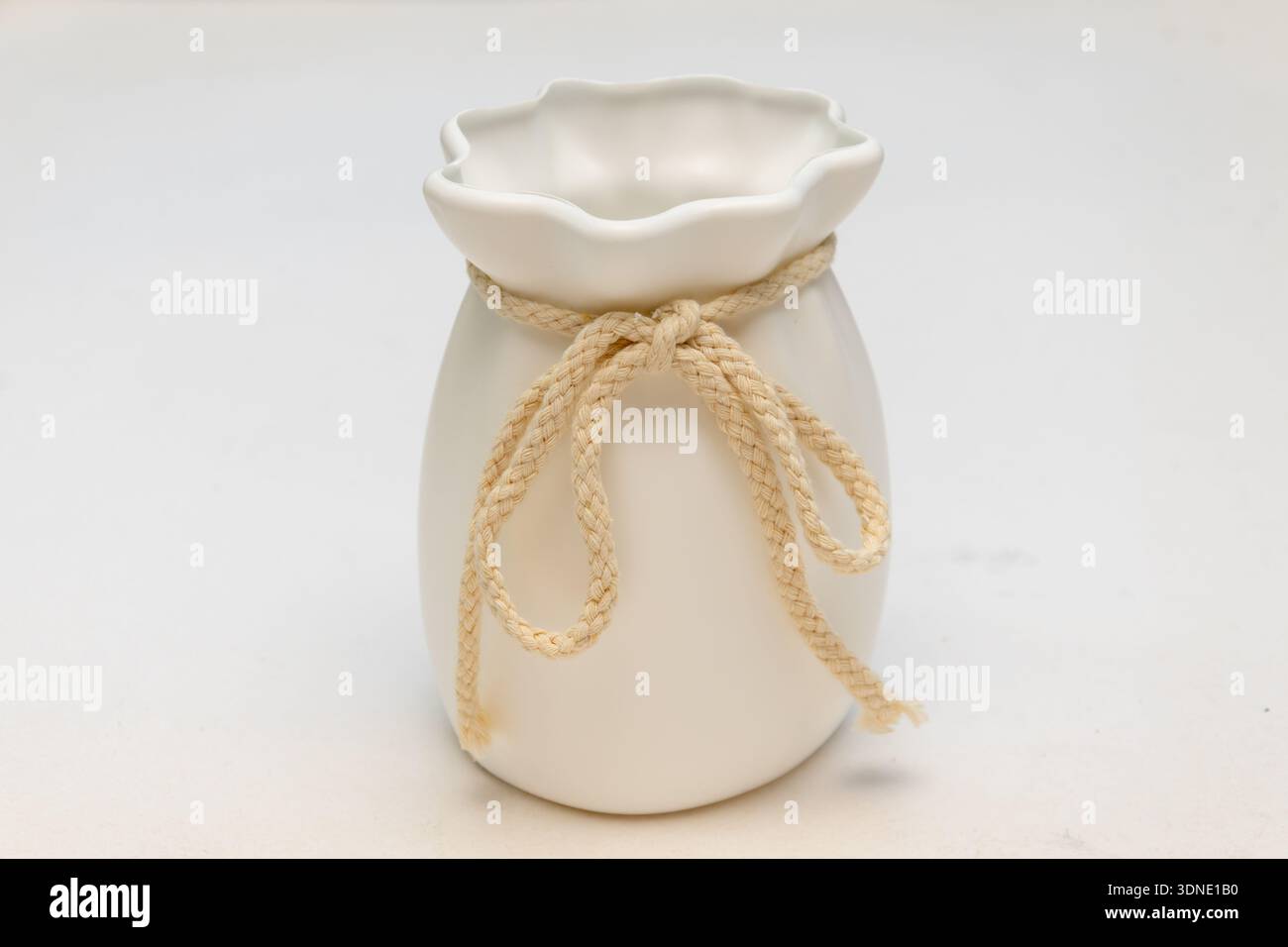 Vaso in ceramica bianca legato con corda decorativa su sfondo chiaro Foto Stock