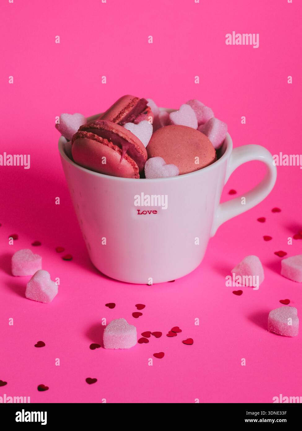 L'amore in una tazza - l'idea del biglietto di San Valentino. Macaron rosa e cuori di zucchero in una tazza con scritta "LOVE" su sfondo rosa Foto Stock