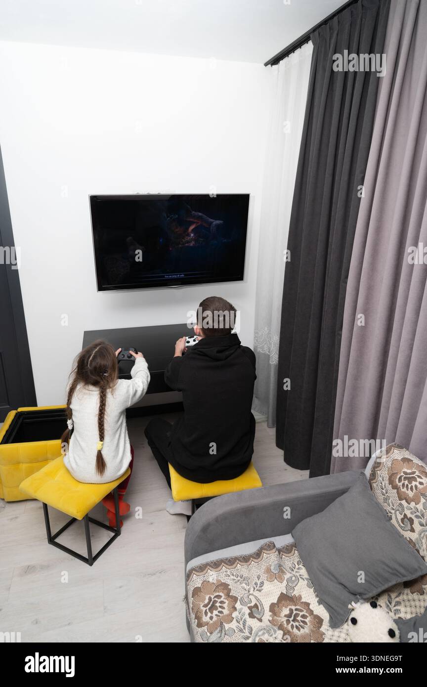 I fratelli e sorelle trascorrono insieme una divertente serata di gioco in un accogliente soggiorno, creando ricordi pieni di risate e amichevoli competizioni durante l'inverno Foto Stock