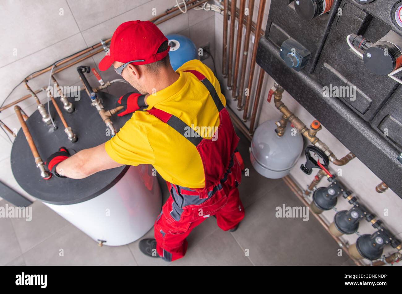 Un lavoratore sta riparando i tubi in un locale di servizio mentre si trova vicino a uno scaldacqua. Foto Stock