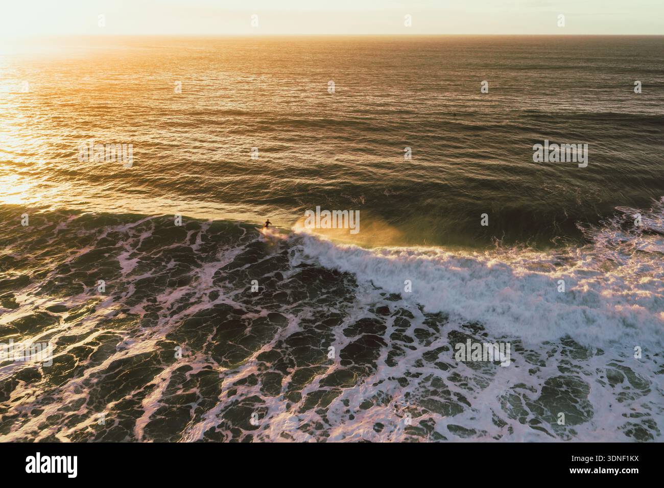 Vista aerea della luce dorata del sole che baciano le onde schiumose mentre un surfista cavalca la cresta, Bidart, Nouvelle-Aquitaine, Francia. Foto Stock
