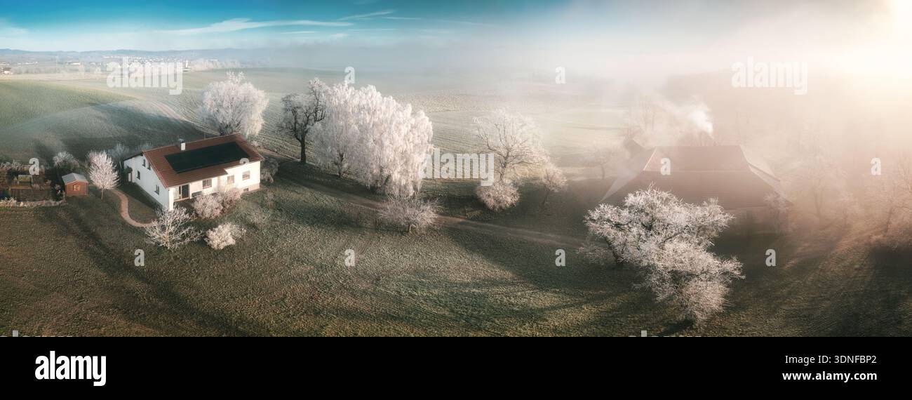 Casa rurale in un magico paesaggio ghiacciato. Vista aerea panoramica del paese delle meraviglie d'inverno con una casa, cielo blu e parrucchiere su alberi e prati Foto Stock