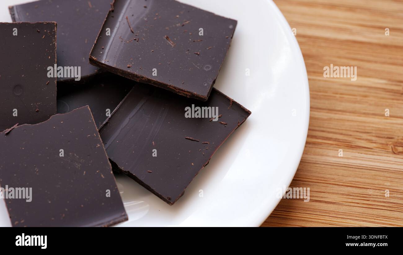 Pezzi di cioccolato fondente rotti su un piatto bianco. Primo piano. Foto Stock