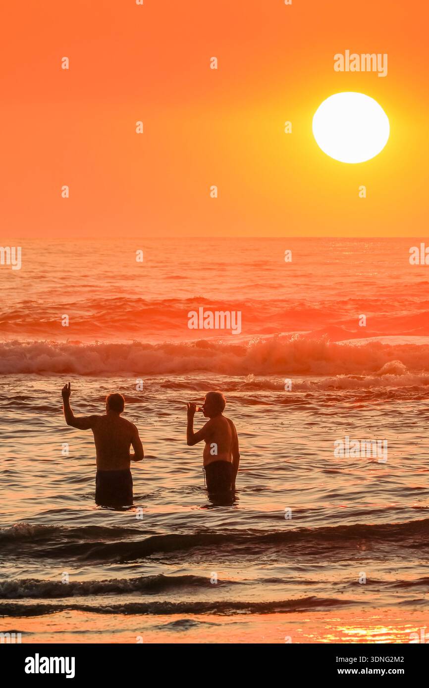 Due amici maschi che si godono le birre al tramonto sulla spiaggia di Guiones vicino a Garza. Guiones, Nosara, Guancaste, Costa Rica. Foto Stock