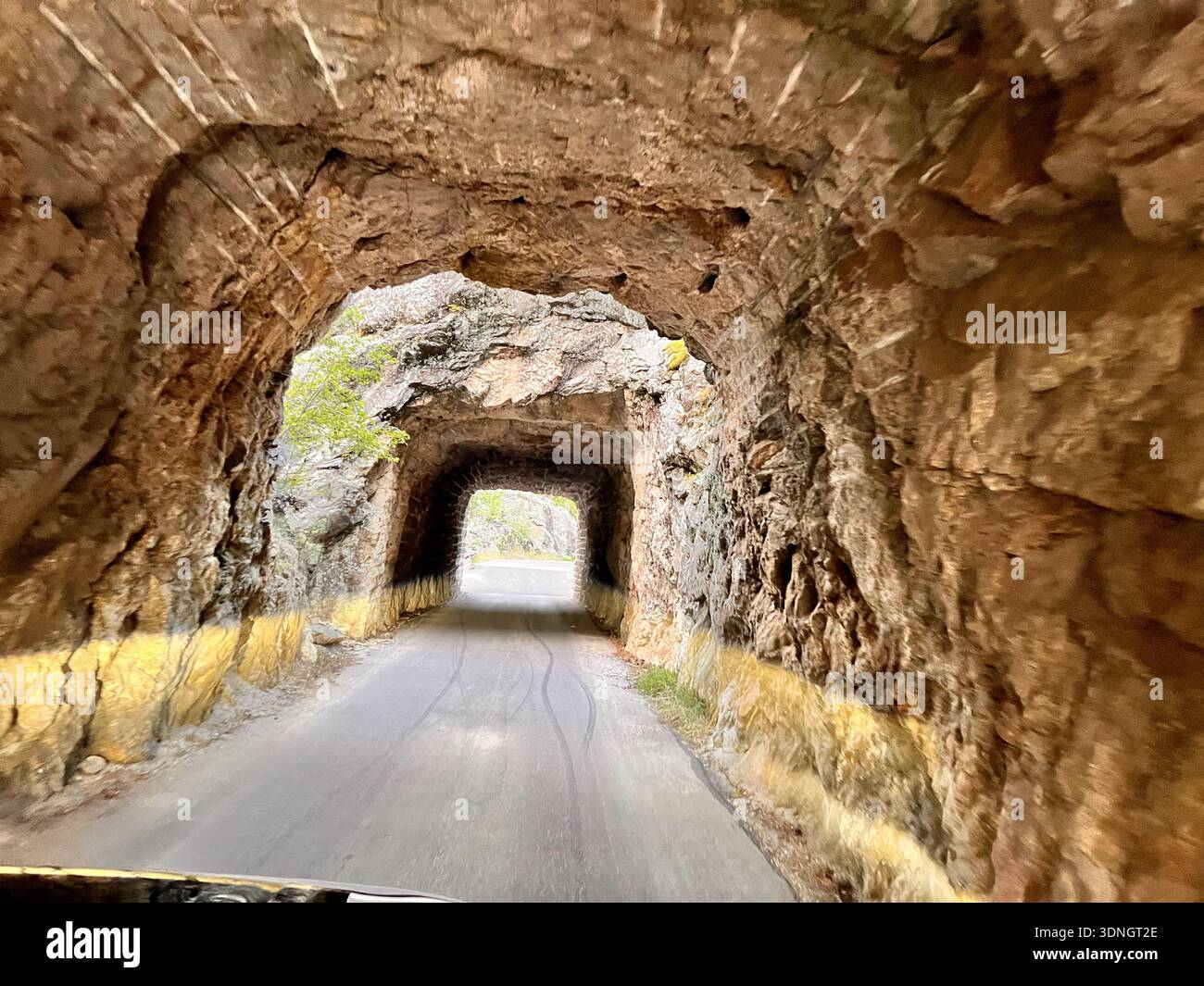 Tunnel scavato nella roccia con ingresso illuminato dal sole e stretta strada di montagna - Immagine stock catturata con smartphone
