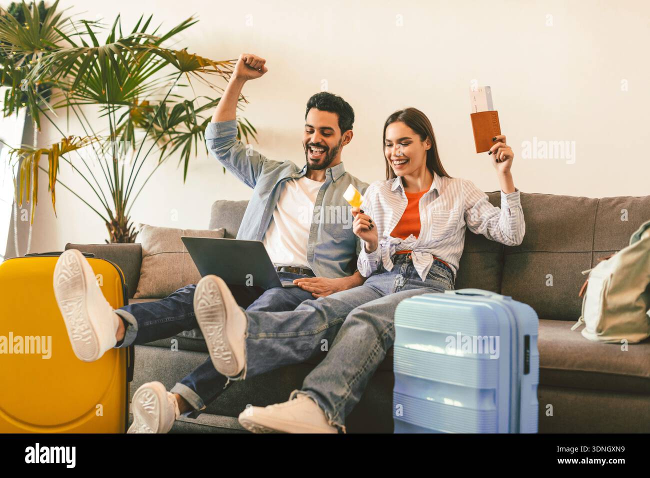 Coppia felice prenotazione hotel online con computer portatile e carta di credito, seduta con valigie, passaporti e biglietti Foto Stock