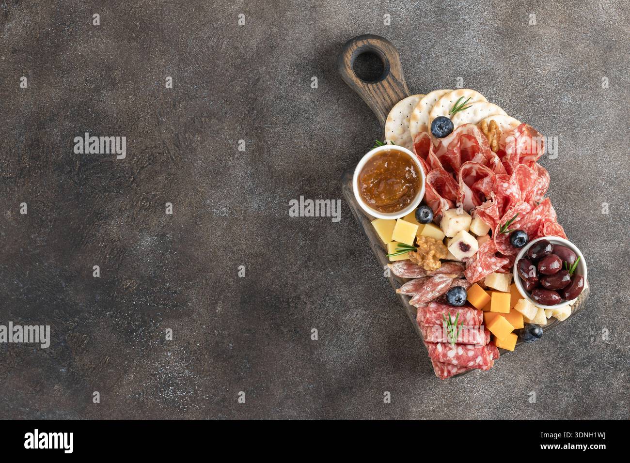 Tagliere di salumi con salame, formaggio, cracker, olive e noci su sfondo scuro. Vista dall'alto. Spazio per copiare Foto Stock