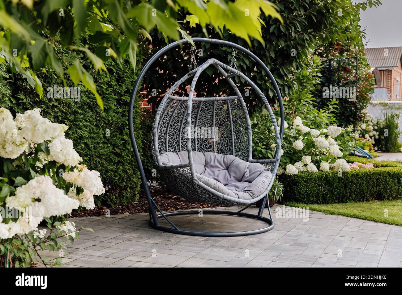 Sedia a uovo appesa sul patio nel lussureggiante giardino con ortensie fiorite Foto Stock