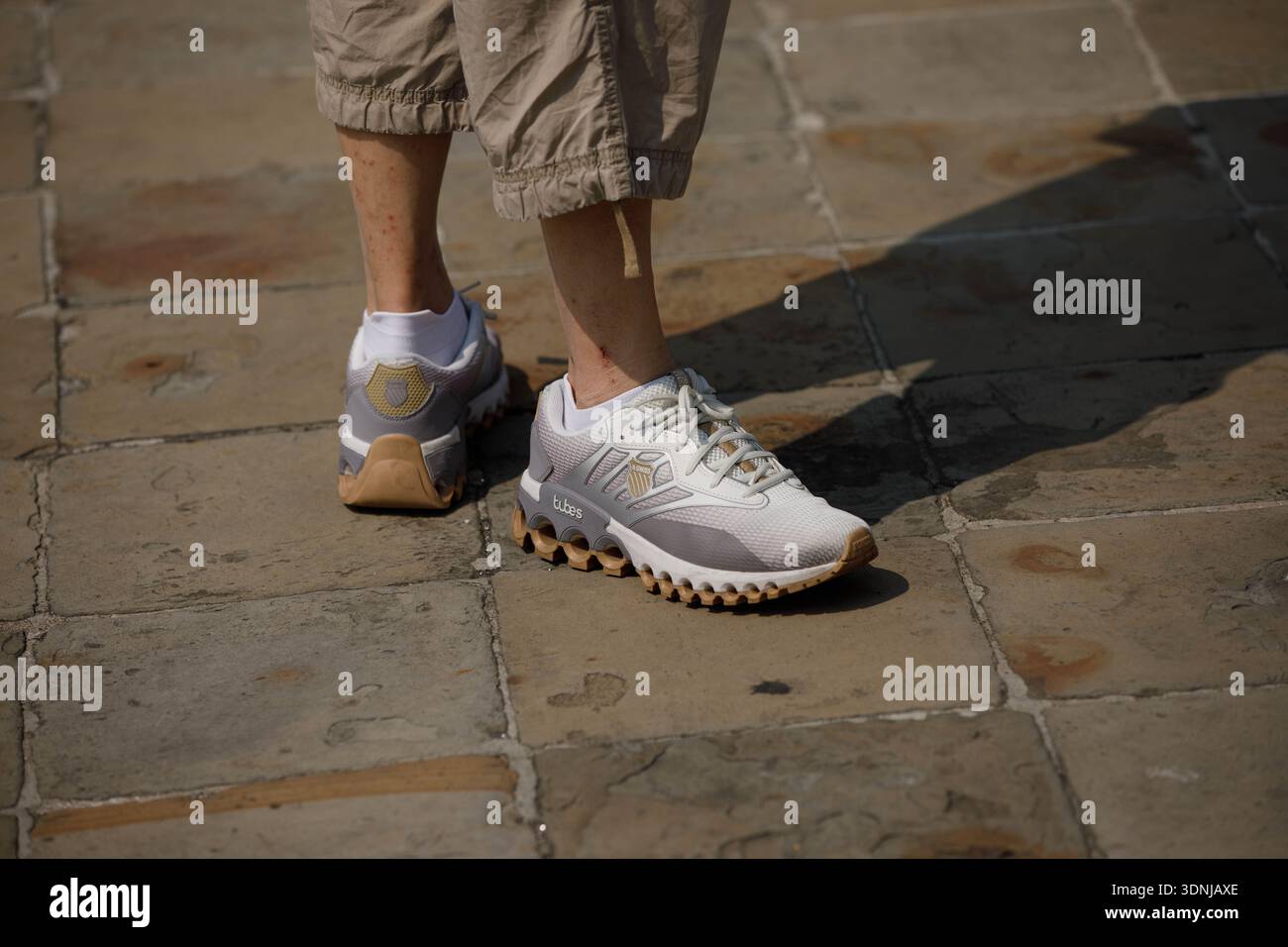 BANGKOK, THAILANDIA - 19 GENNAIO 2026: Turista in pantaloncini corti con scarpe bianche K-Swiss in piedi su un pavimento in pietra, vista ad angolo alto Foto Stock