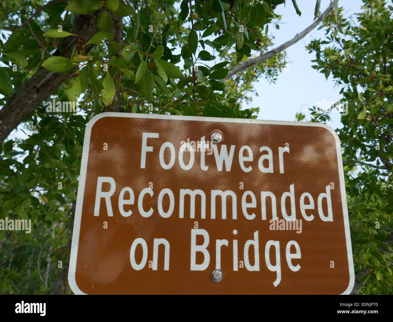 Si consiglia di indossare scarpe sul cartello del ponte con piante tropicali sullo sfondo Foto Stock