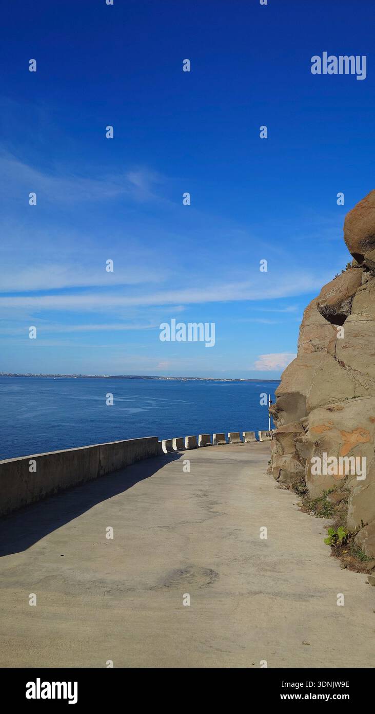 Strada costiera panoramica accanto a massicce formazioni rocciose di basalto che si affacciano sull'oceano blu sotto un cielo limpido nelle isole Penghu, Taiwan. Foto Stock