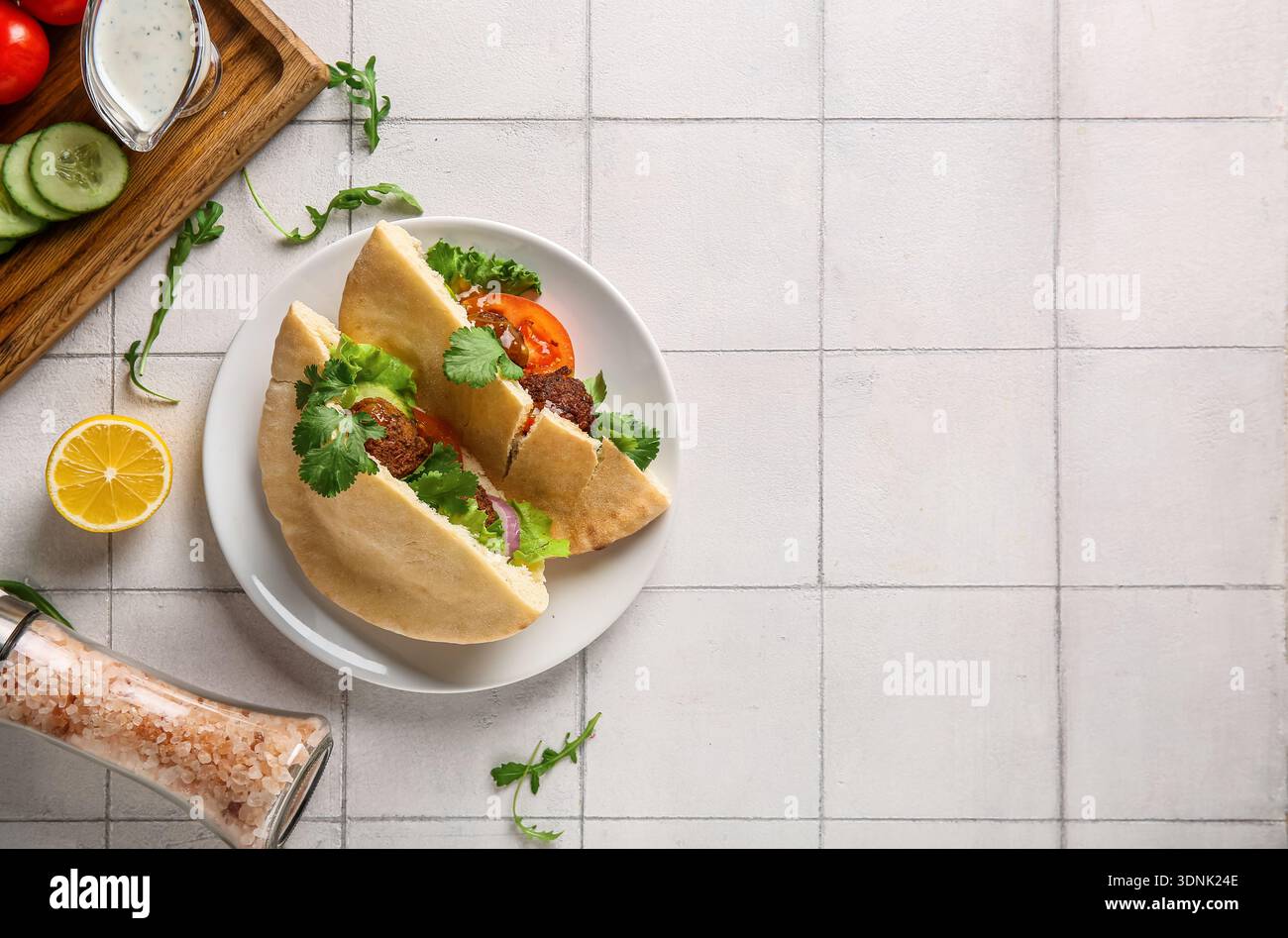 Piatto di deliziose pitas con falafel e verdure fresche su sfondo piastrellato bianco Foto Stock