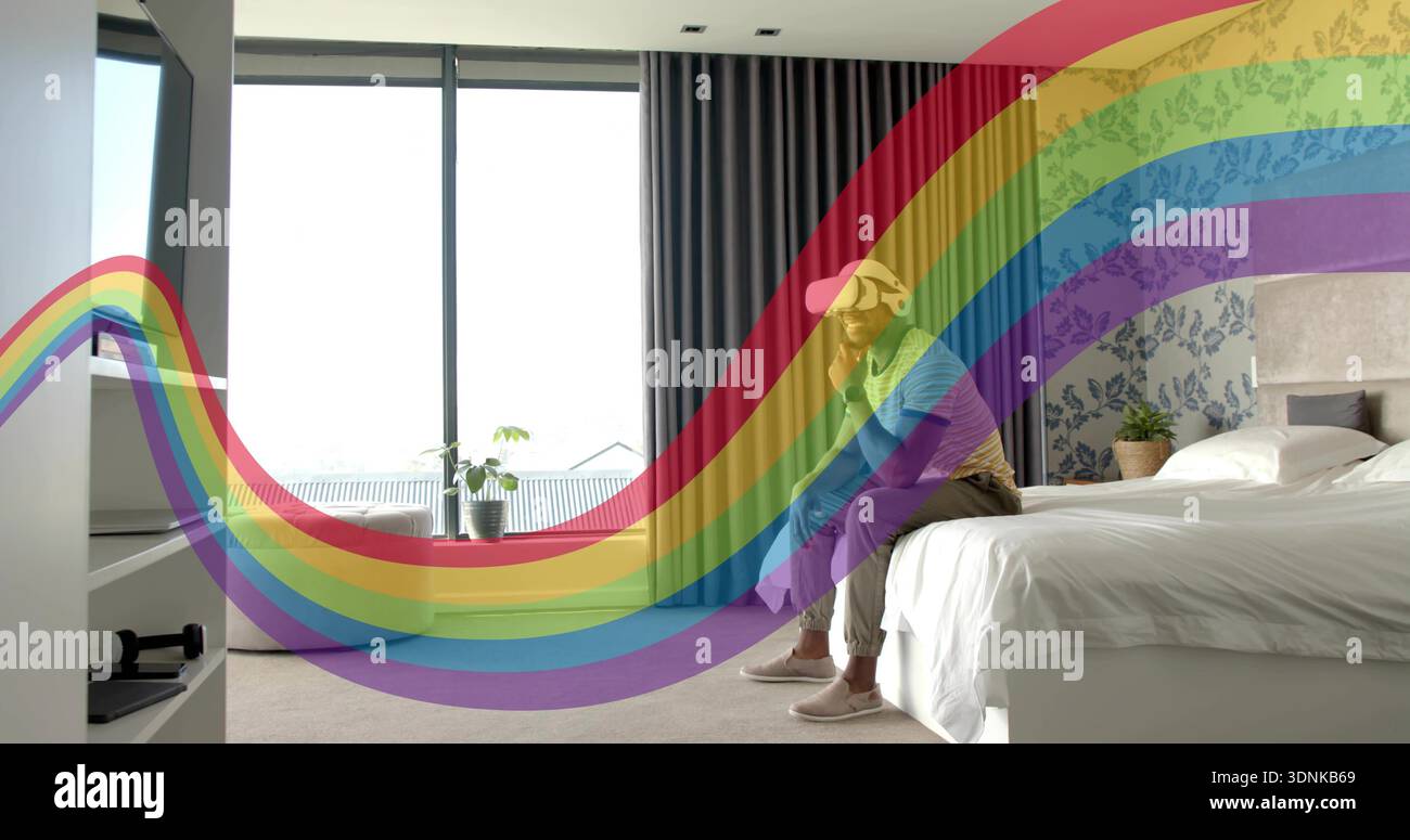 Tenendo in mano un uomo che indossa un cappellino da baseball, seduto sul letto accanto alla finestra con rivestimento arcobaleno, spazio per fotocopie Foto Stock