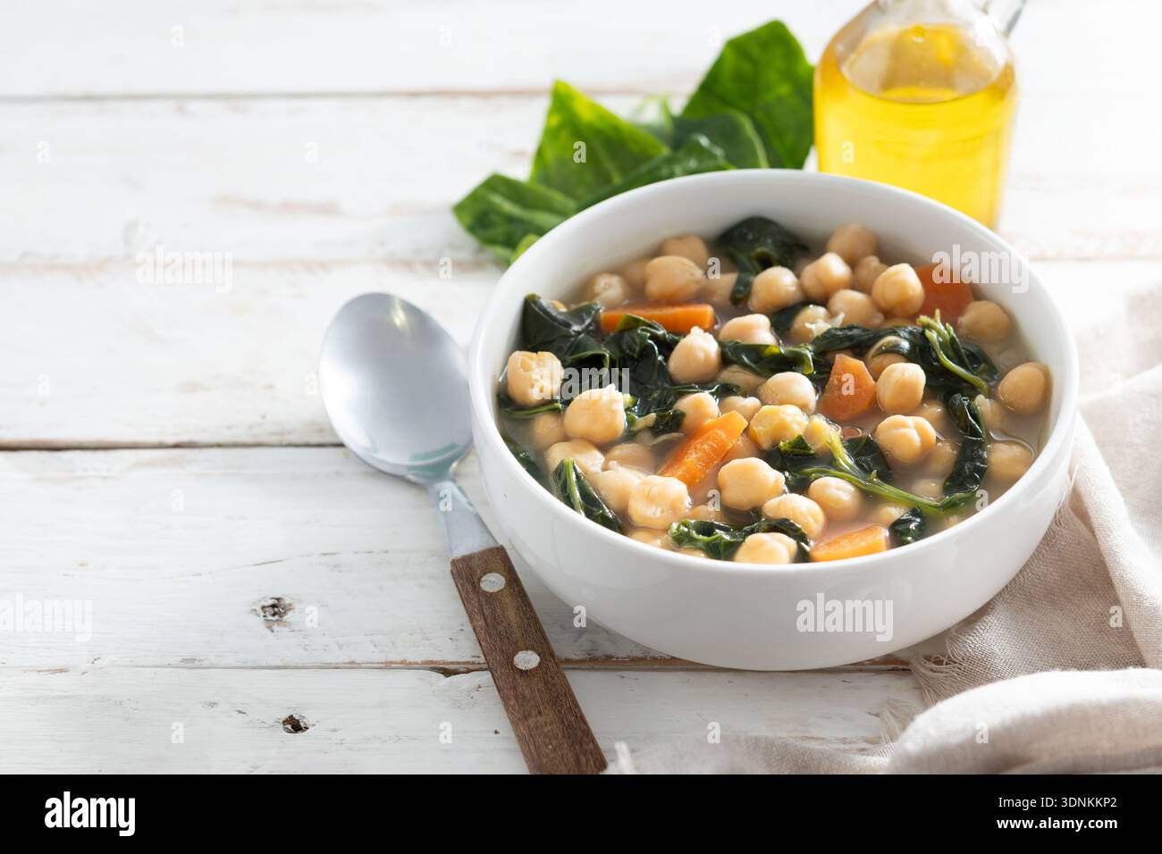 Zuppa fatta in casa di ceci e spinaci con carote affettate servita in una ciotola bianca su un tavolo di legno Foto Stock