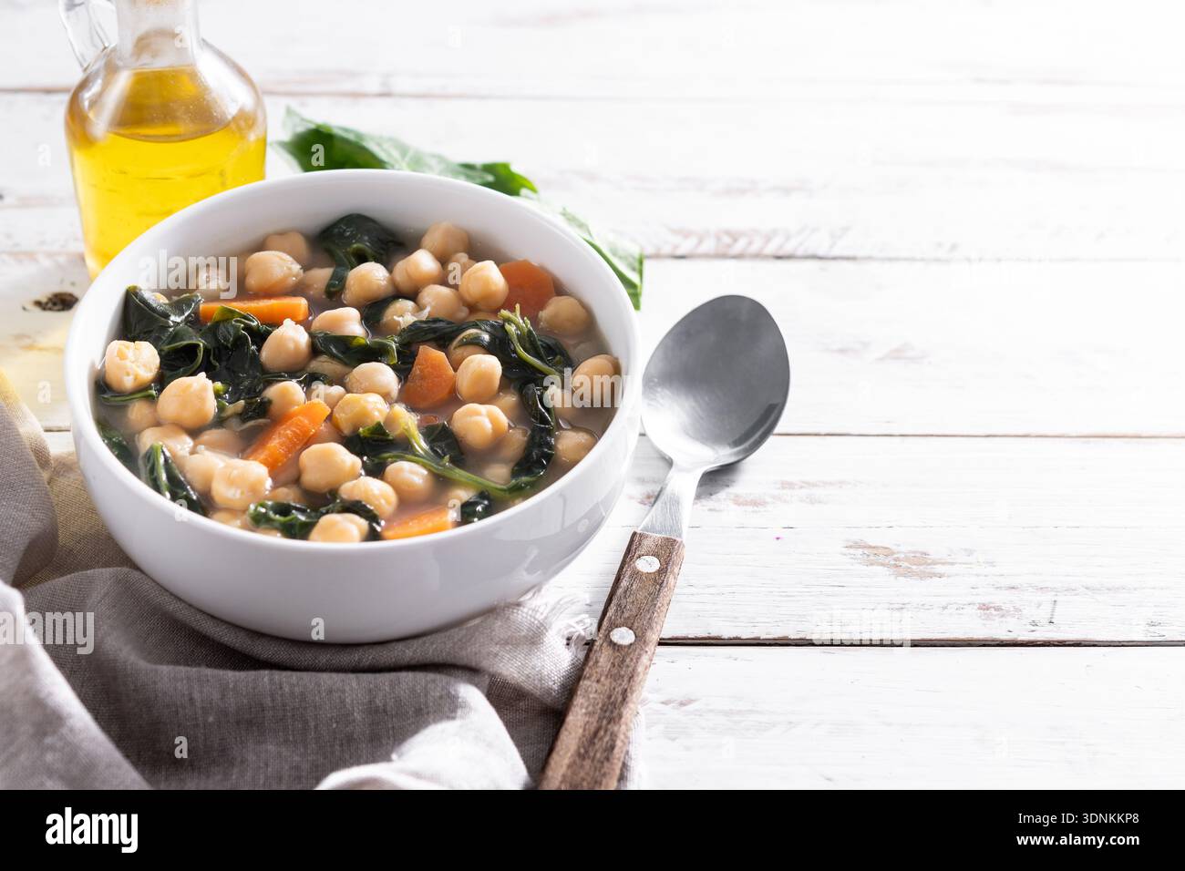Zuppa fatta in casa di ceci e spinaci con carote affettate servita in una ciotola bianca su un tavolo di legno Foto Stock