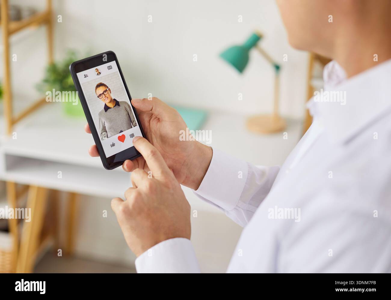 Persona che utilizza l'app per appuntamenti per smartphone per aggiungere un "mi piace" a un profilo con l'icona del cuore in primo piano Foto Stock