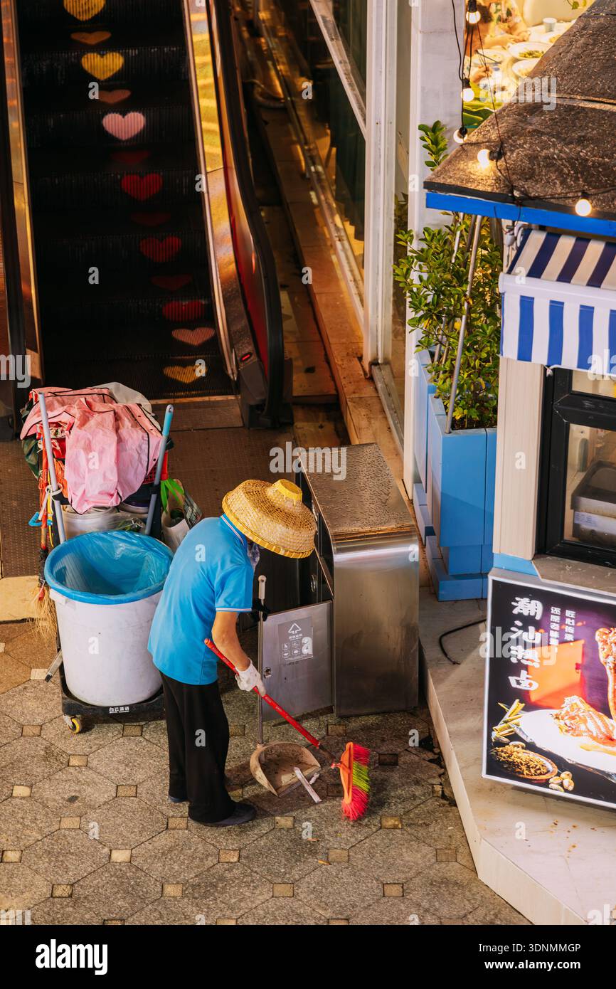 Pulitore della strada che indossa un cappello di bambù che spazza il pavimento di notte a Sanya Foto Stock