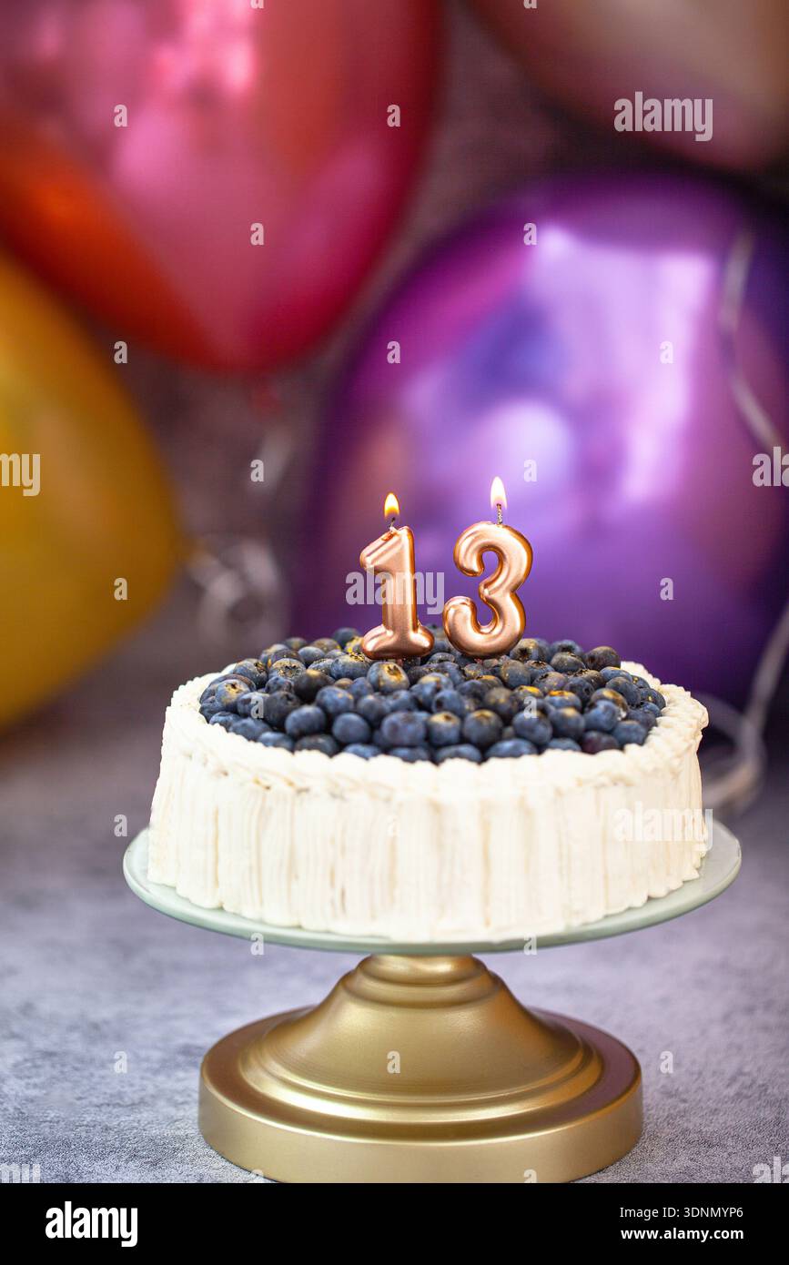 Torta di compleanno ai mirtilli con numero di candels 13 per festeggiare gli adolescenti con palloncini colorati sullo sfondo Foto Stock