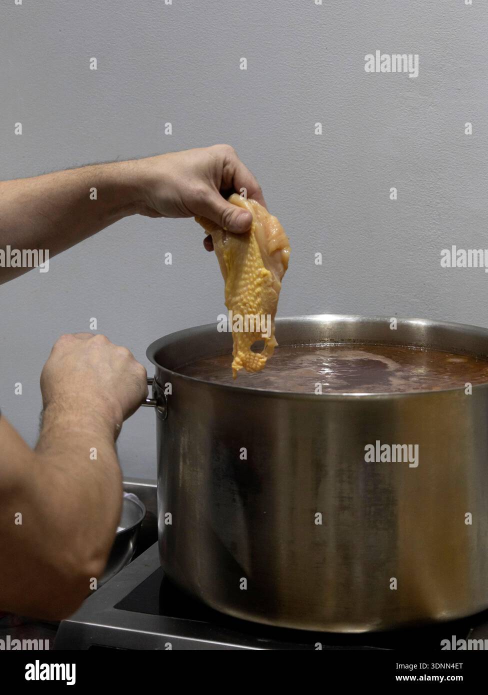 Lo chef prepara un brodo di pollo in una pentola di acciaio inossidabile, preparando una base per zuppa Foto Stock