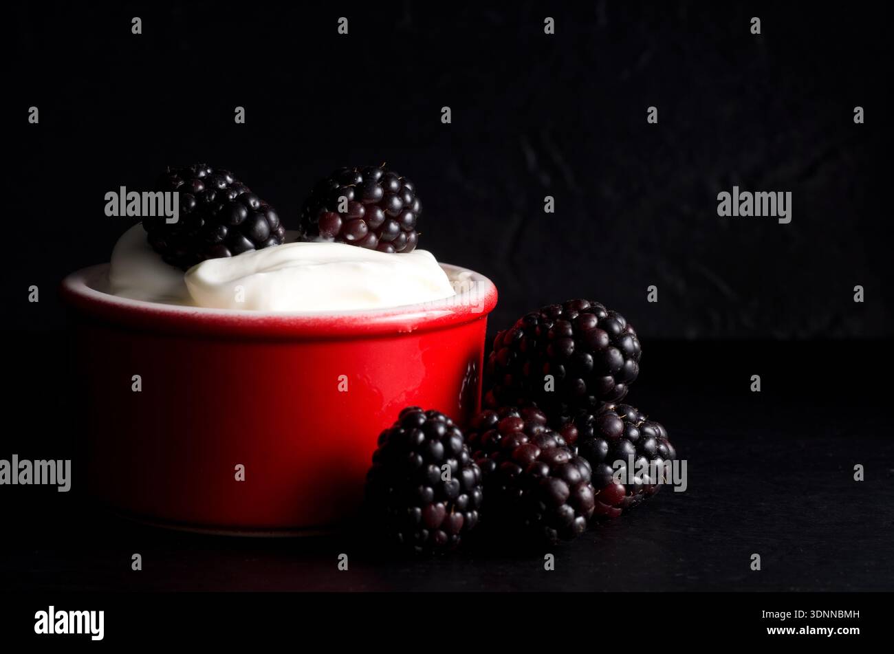 Primo piano di Blackberries con yogurt alla vaniglia nel Red Bowl con sfondo nero orizzontale Foto Stock