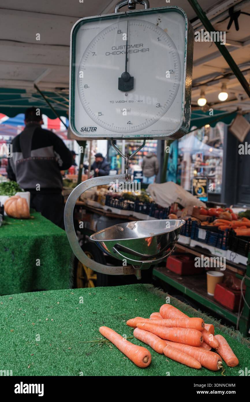 Bilance tradizionali e carote in una bancarella di mercato in un mercato di Londra, che mostra le attività quotidiane di vendita al dettaglio. Foto Stock