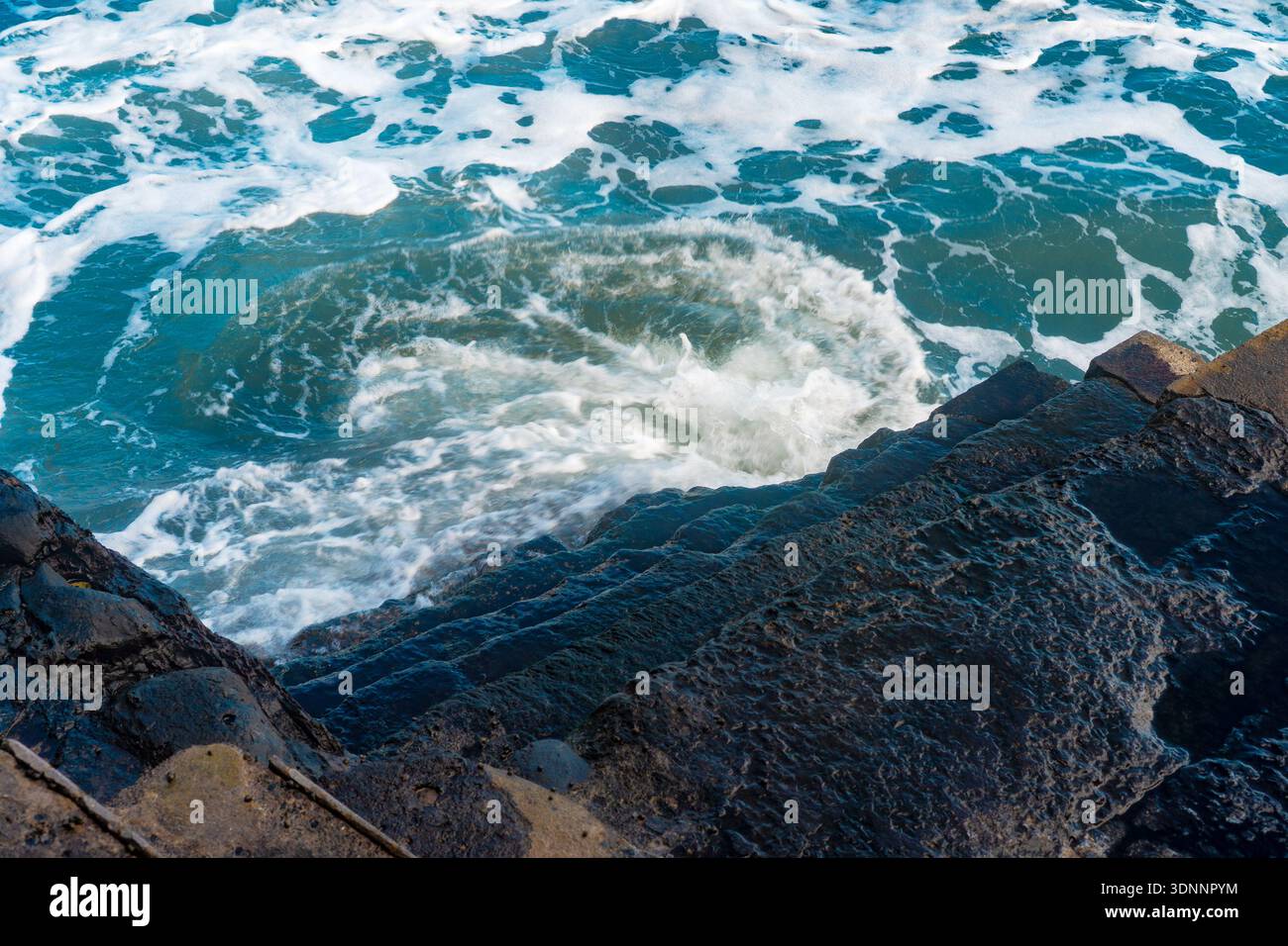 Vista ad alto angolo delle onde dell'oceano che ruotano dalle scale di pietra. Foto Stock