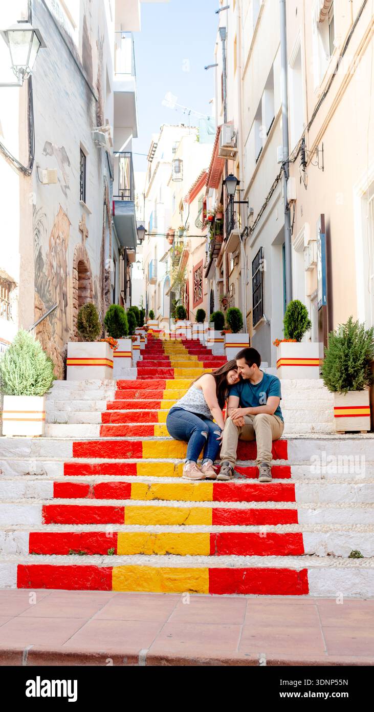 Una coppia gode di un momento tranquillo sulle vibranti scale dipinte nei colori della bandiera spagnola, situato nell'affascinante cittadina di Calpe, Alicante. La zona è viva Foto Stock