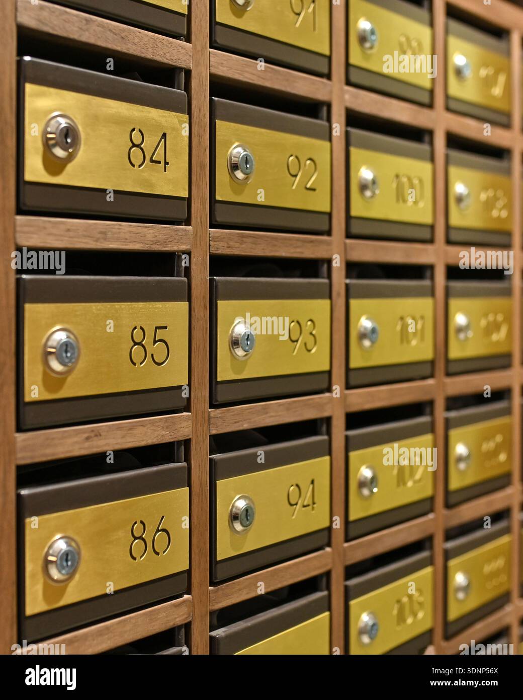 Primo piano di cassette postali in ottone vintage con serrature a combinazione disposte su una parete in legno. Ogni scatola è numerata e presenta un classico ed elegante deposito postale Foto Stock