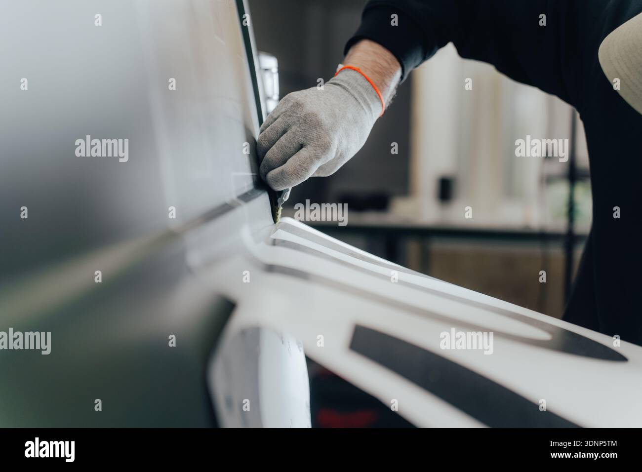Un lavoratore qualificato in un'officina automobilistica si concentra sul branding e la personalizzazione dei veicoli. Il processo prevede la realizzazione manuale, evidenziando l'oggetto Foto Stock