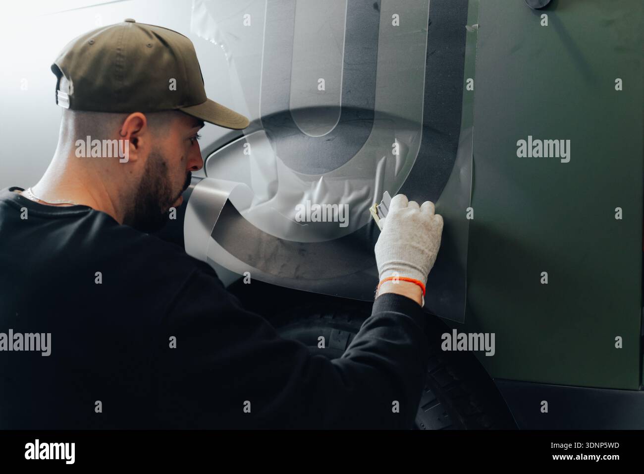 Un lavoratore esperto applica un progetto personalizzato a un veicolo in un'officina automobilistica. L'immagine mette in evidenza la cura manuale necessaria per la personalizzazione automatica Foto Stock