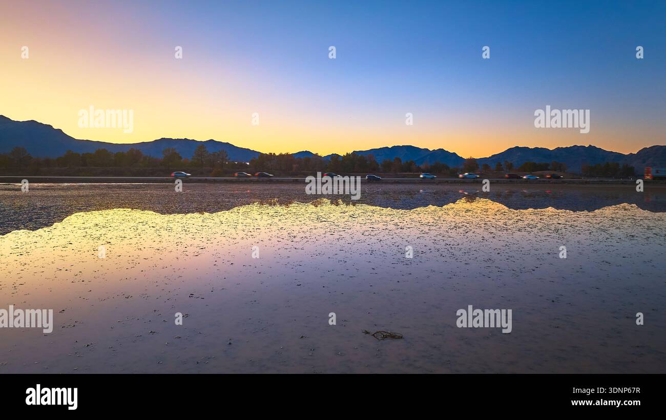 Golden Hour Lake Reflections with Mountains and Cars at Sunset Foto Stock