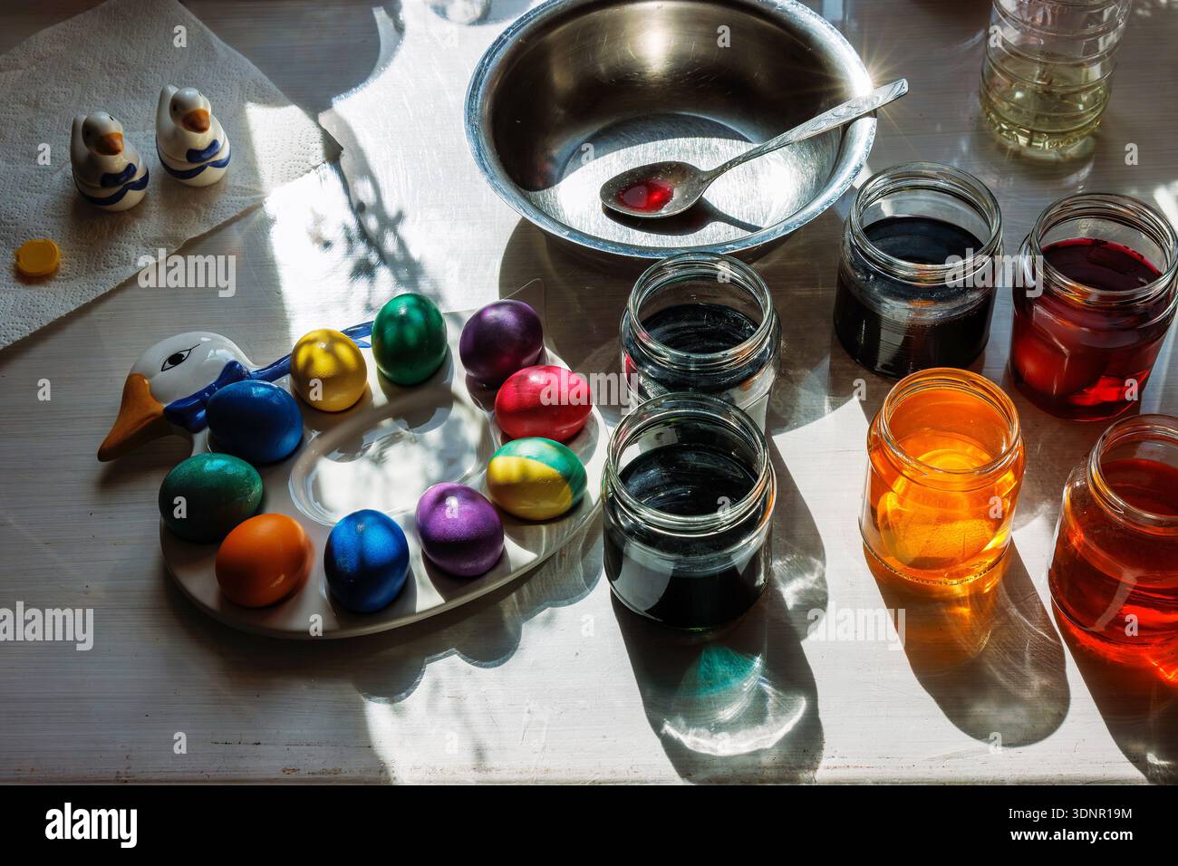 Le uova colorate riposano su un piatto a forma di anatra accanto ai vasetti di vetro di colorante liquido sul tavolo della cucina Foto Stock