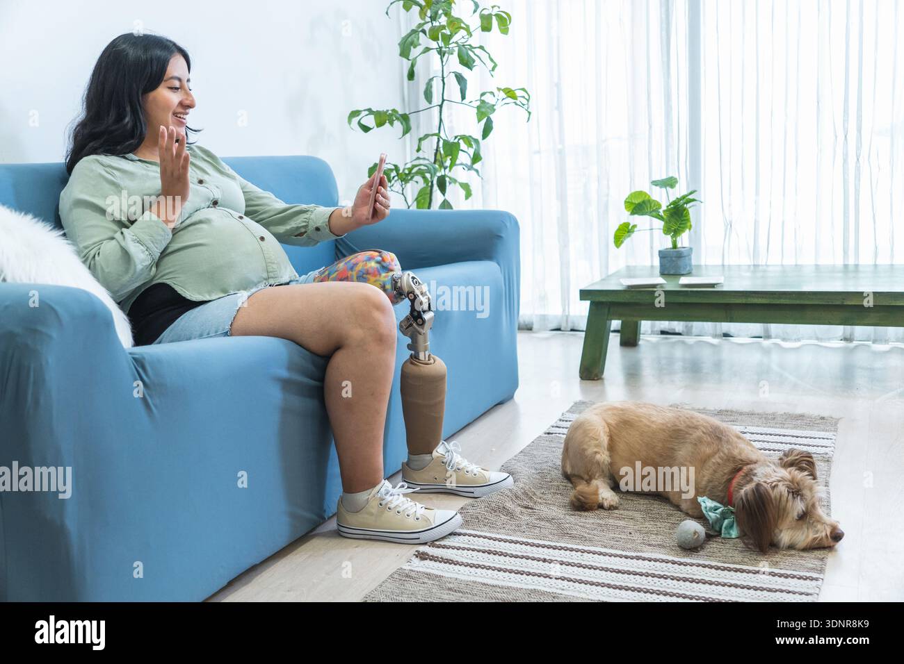 Donna incinta con protesi alle gambe che videochiama a casa con il suo cane Foto Stock