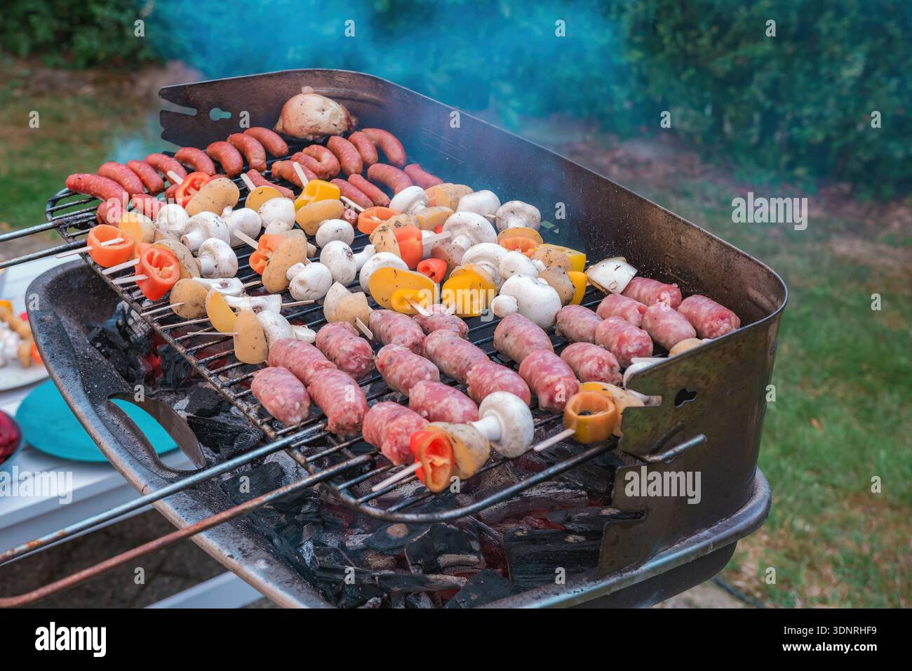 L'immagine mostra un barbecue con una varietà di carni e verdure su una griglia direttamente esposta al calore dei carboni. Foto Stock