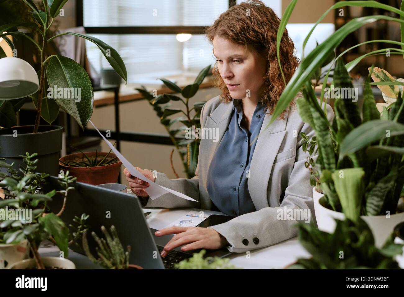 Giovane donna che analizza i documenti mentre lavora su un notebook Foto Stock