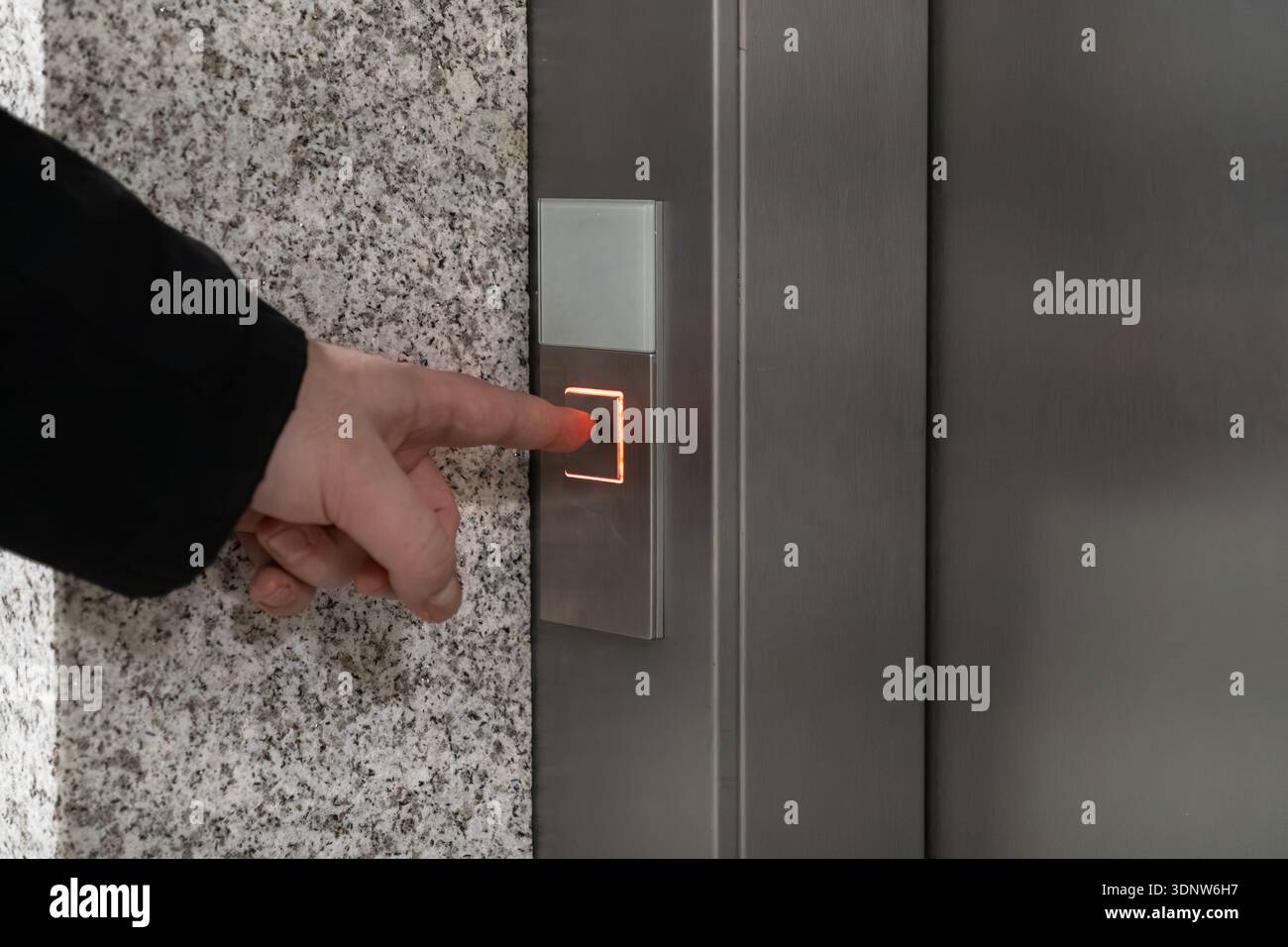 Primo piano di una mano umana attivando un pulsante di chiamata luminoso su un elegante pannello di controllo metallico dell'ascensore, che rappresenta tecnologia avanzata e vert liscio Foto Stock