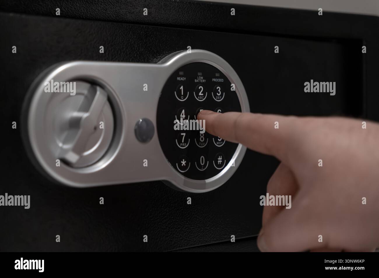 Primo piano di una mano che preme i numeri su un'elegante cassaforte elettronica nera con una tastiera argentata, che rappresenta la conservazione sicura di documenti importanti e documenti Foto Stock