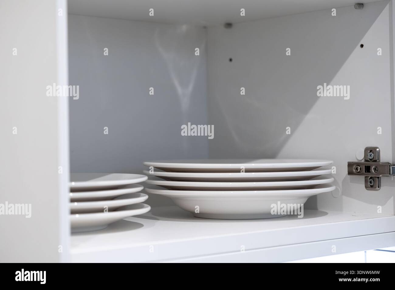 Primo piano di piatti in ceramica bianca luminosi impilati in pile ordinate all'interno di un armadietto da cucina moderno e organizzato, che enfatizza la praticità e l'eleganza della casa Foto Stock