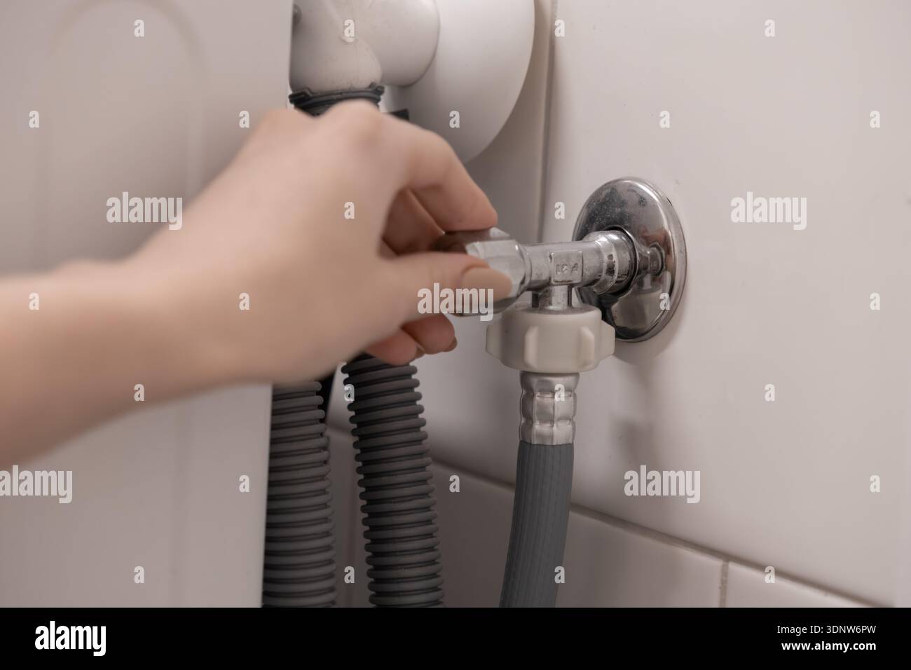 Primo piano della mano di una persona regolando con attenzione una valvola dell'acqua cromata lucida, gestendo il collegamento di alimentazione cruciale per la riparazione delle tubazioni domestiche e m Foto Stock