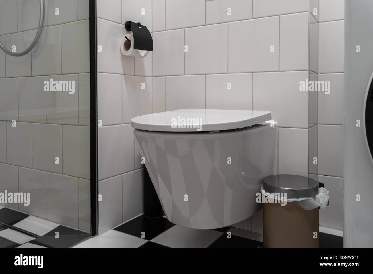 I bagni interni moderni e puliti sono dotati di WC a parete, dispenser di carta igienica nera e pavimento a scacchi, per offrire un moderno hy personale Foto Stock