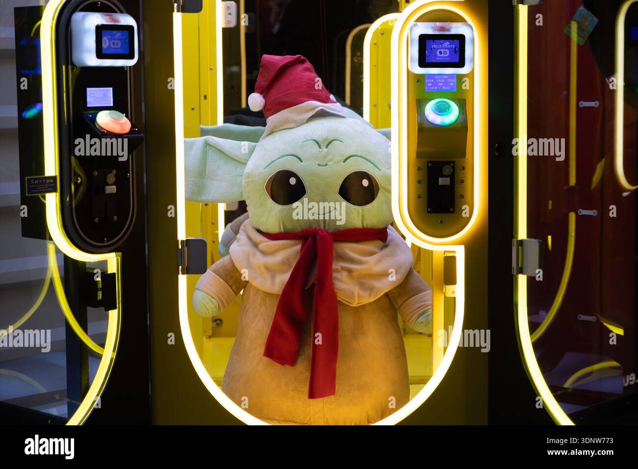 Cracovia, Polonia - 30 novembre 2025: Peluche Grogu (Baby Yoda), cappello di Babbo Natale, sciarpa rossa, sala giochi a premi illuminata, incarna la cultura popolare festosa Foto Stock