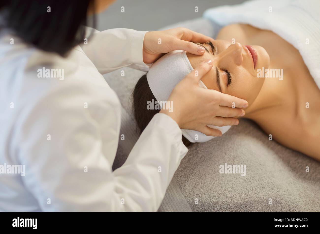 Estetista che fa un massaggio facciale rilassante esercitando una leggera pressione sui muscoli facciali della donna Foto Stock